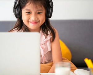 girl sitting at home on her couch with headphones on a video chat with a speech therapist